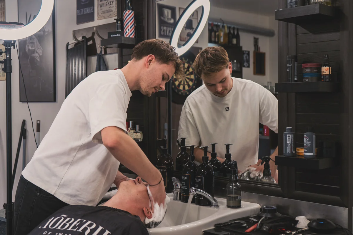 Mytí vlasů u umyvadla, barbér a odraz v zrcadle – Notorious Barbershop Kyjov